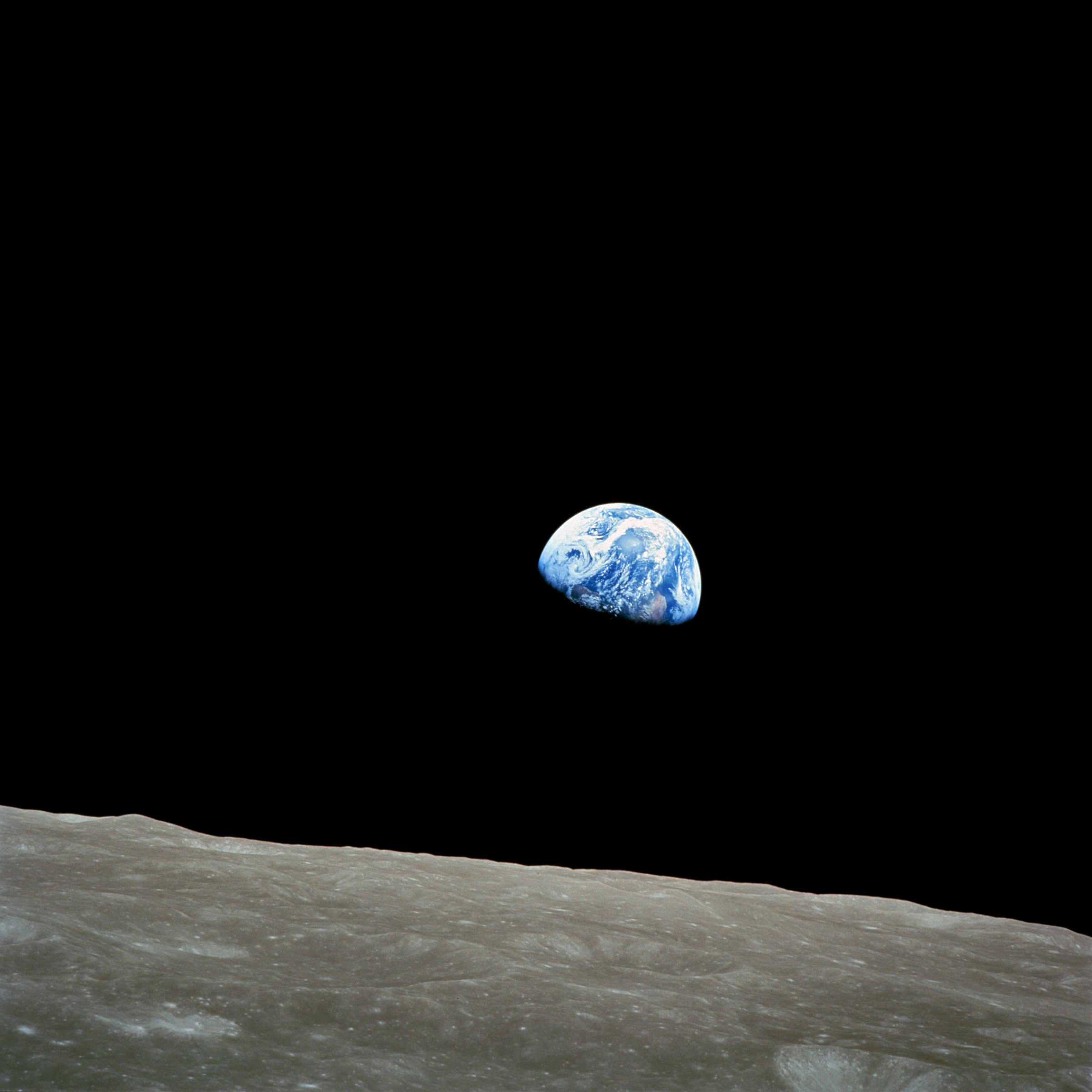 A view of Earth rising over the lunar horizon, with a dark space background and a textured surface of the Moon in the foreground.